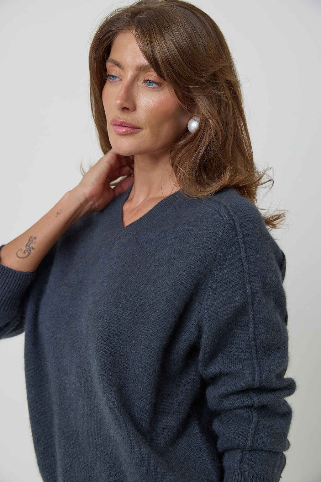 A woman wearing a dark slate blue knit cashmere sweater, shown from the chest up against a plain light gray studio background.