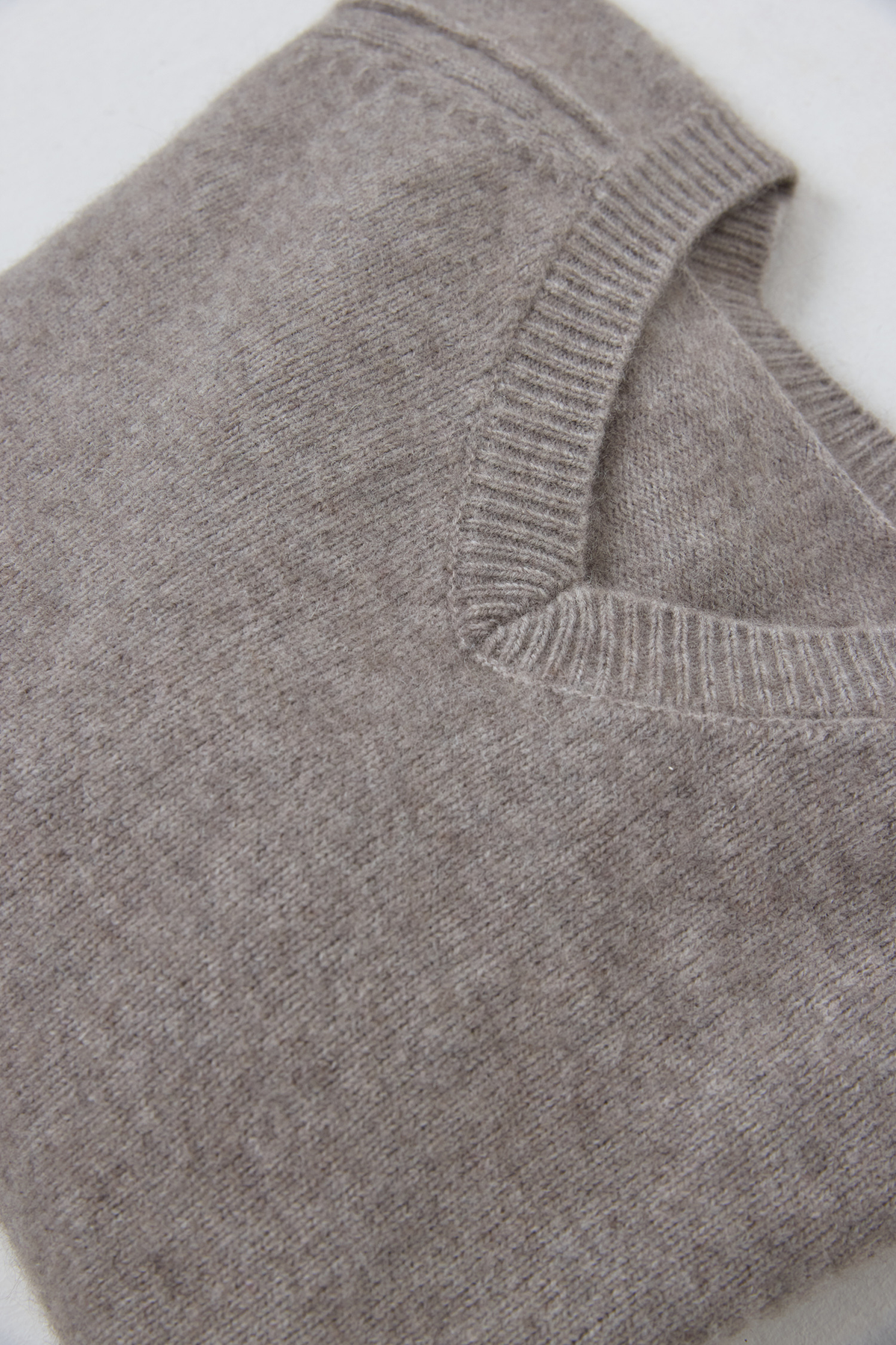 Close-up of a folded cashmere knit sweater in a heather taupe grey color, showing the ribbed v-neck collar.