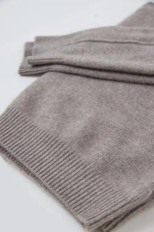 A folded cashmere knit sweater in a heathered taupe-grey colour, showing the ribbed cuff and soft texture on a plain white background.