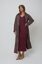A woman modelling a long brown genuine suede coat over a ribbed burgundy wool midi dress, paired with beige pointed-toe heels, against a light grey studio background.